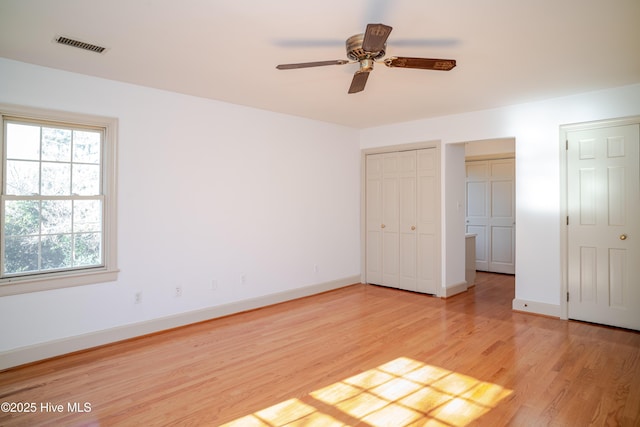 unfurnished bedroom with two closets, ceiling fan, and light wood-type flooring