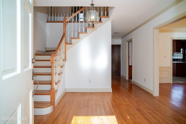 stairway featuring ornamental molding, a chandelier, sink, and wood-type flooring