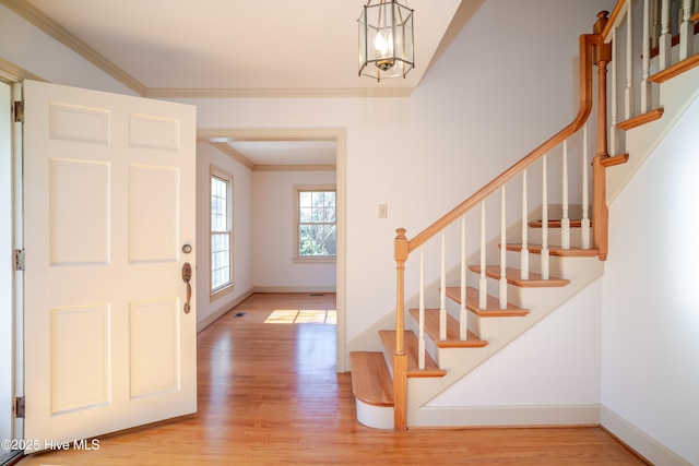 entrance foyer with ornamental molding, a chandelier, and light hardwood / wood-style floors