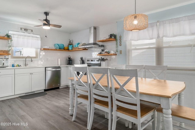 kitchen with white cabinetry, hanging light fixtures, dishwasher, wall chimney range hood, and backsplash