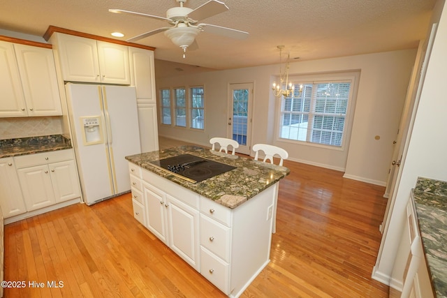 kitchen with black electric cooktop, white refrigerator with ice dispenser, light wood-style floors, white cabinets, and hanging light fixtures