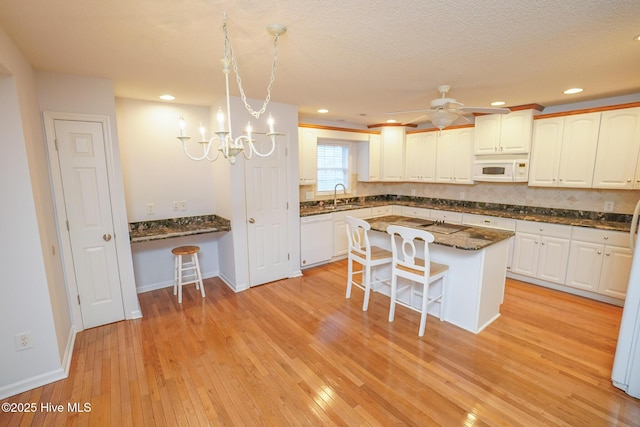 kitchen featuring white appliances, a breakfast bar area, a sink, and white cabinets