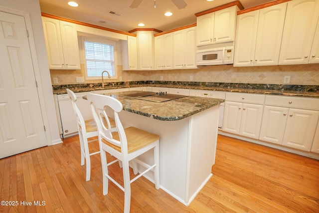 kitchen featuring white appliances, visible vents, a kitchen island, light wood-style floors, and a sink