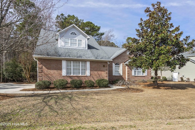 view of front of house featuring a shingled roof, brick siding, and a front lawn