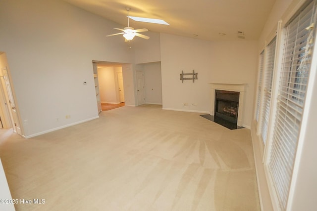 unfurnished living room with light colored carpet, a fireplace with flush hearth, ceiling fan, high vaulted ceiling, and baseboards