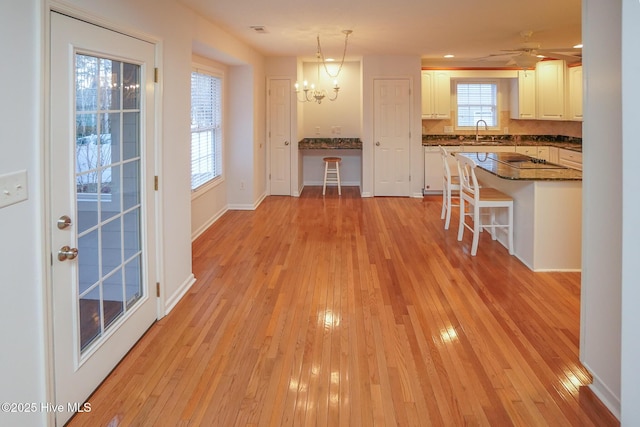 interior space featuring light wood finished floors, a kitchen bar, white cabinetry, pendant lighting, and a sink