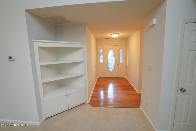 doorway to outside featuring baseboards, visible vents, light colored carpet, light wood-style flooring, and built in shelves