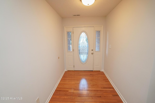 doorway to outside featuring light wood finished floors, baseboards, visible vents, and a textured ceiling