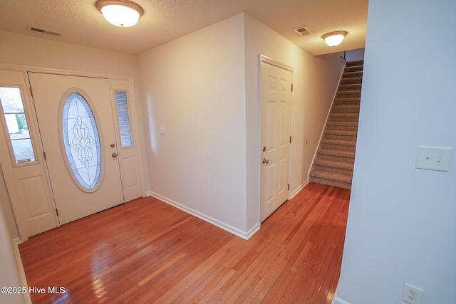 entrance foyer with light wood-style floors, visible vents, a textured ceiling, and stairs