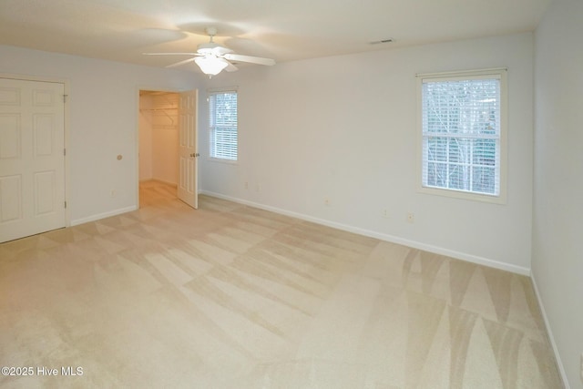 unfurnished bedroom featuring visible vents, a spacious closet, light carpet, ceiling fan, and baseboards