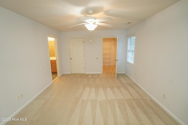 unfurnished bedroom with a walk in closet, a closet, light colored carpet, ensuite bathroom, and baseboards