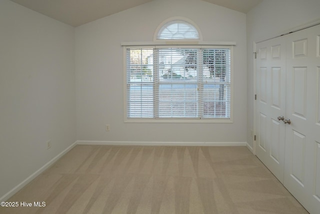 spare room with light carpet, lofted ceiling, and baseboards