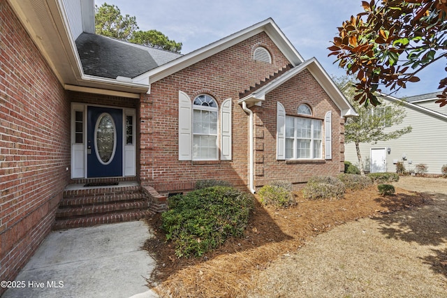 property entrance featuring brick siding and a shingled roof