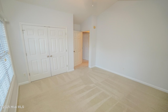 unfurnished bedroom featuring vaulted ceiling, a closet, light carpet, and baseboards