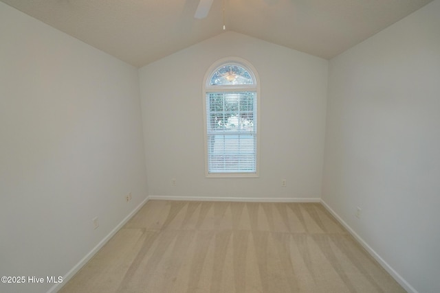 empty room with a ceiling fan, light colored carpet, vaulted ceiling, and baseboards