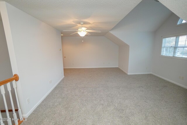 bonus room featuring ceiling fan, a textured ceiling, light carpet, baseboards, and vaulted ceiling