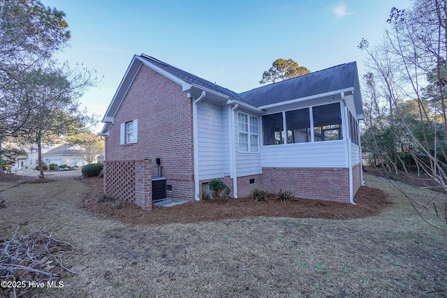 view of side of property with a shingled roof, central AC unit, a sunroom, crawl space, and brick siding