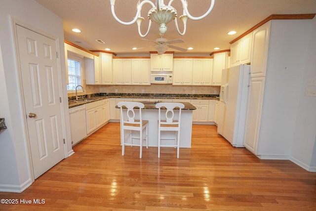 kitchen featuring white appliances, light wood-style floors, a center island, a kitchen bar, and decorative light fixtures