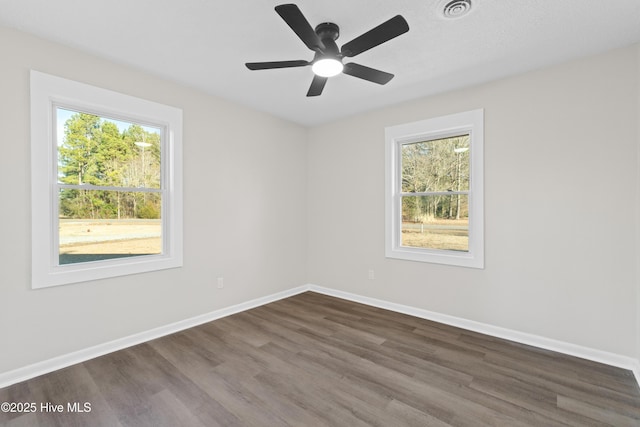 empty room with dark hardwood / wood-style flooring, a wealth of natural light, and ceiling fan