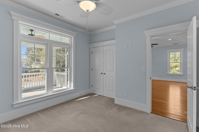 unfurnished bedroom featuring light colored carpet, a closet, ceiling fan, and ornamental molding