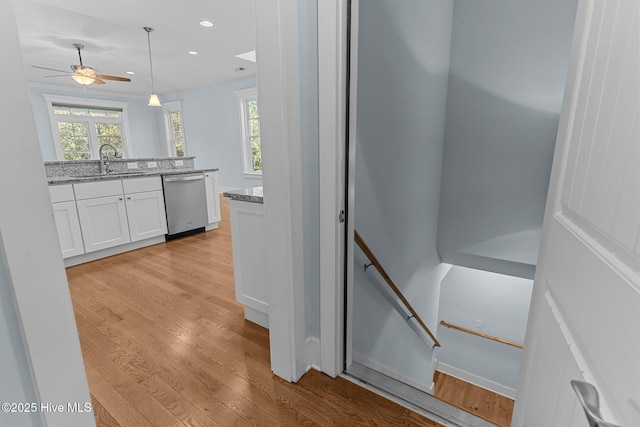 kitchen with light hardwood / wood-style floors, stainless steel dishwasher, white cabinets, decorative light fixtures, and sink