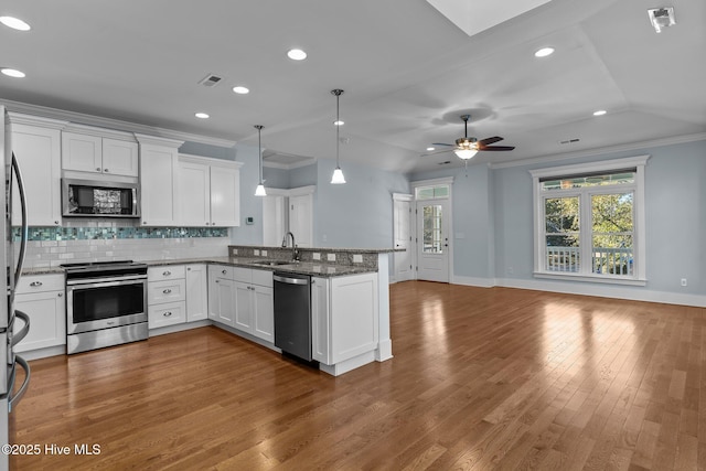 kitchen with kitchen peninsula, appliances with stainless steel finishes, decorative light fixtures, white cabinetry, and dark stone counters