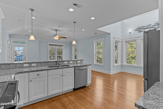 kitchen with sink, stainless steel appliances, light stone counters, and decorative light fixtures