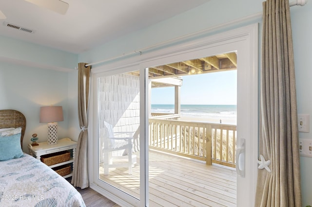 bedroom with a water view, a beach view, light hardwood / wood-style floors, and access to outside