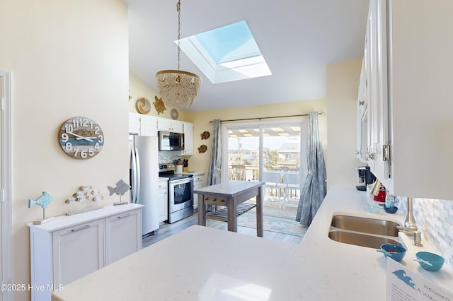 kitchen featuring lofted ceiling with skylight, hanging light fixtures, stainless steel appliances, decorative backsplash, and white cabinets