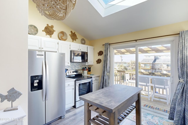 kitchen with lofted ceiling with skylight, white cabinetry, stainless steel appliances, light hardwood / wood-style floors, and decorative backsplash