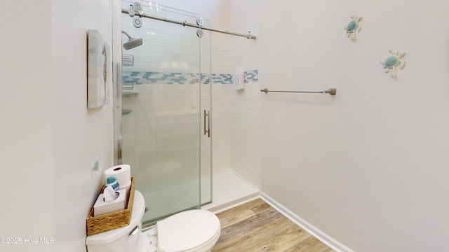 bathroom with hardwood / wood-style flooring, a shower with shower door, and toilet