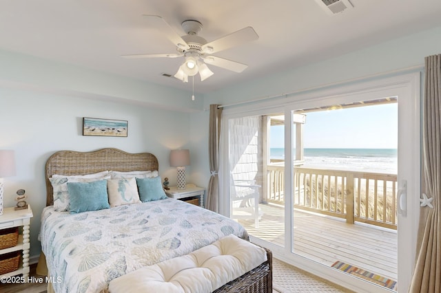 bedroom featuring a view of the beach, access to exterior, ceiling fan, and a water view