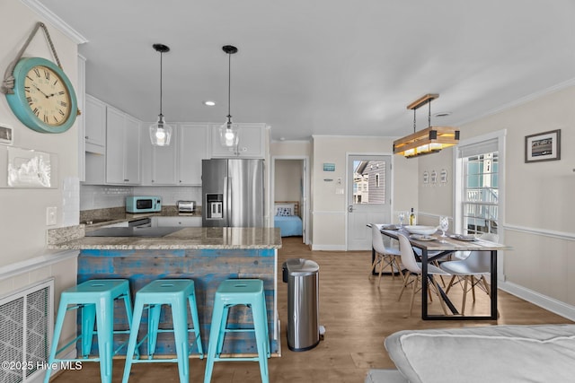 kitchen with wood-type flooring, stainless steel fridge with ice dispenser, hanging light fixtures, a kitchen breakfast bar, and white cabinets