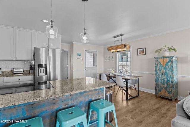 kitchen with pendant lighting, crown molding, stainless steel fridge, white cabinetry, and stone countertops