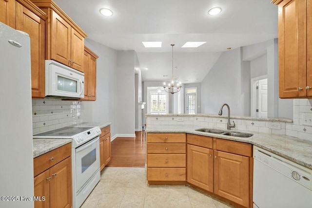 kitchen featuring sink, decorative light fixtures, light stone counters, white appliances, and a skylight