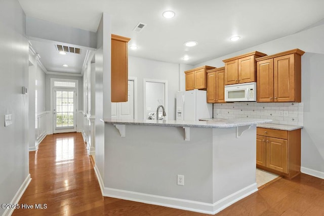 kitchen featuring white appliances, light stone countertops, decorative backsplash, sink, and a breakfast bar area