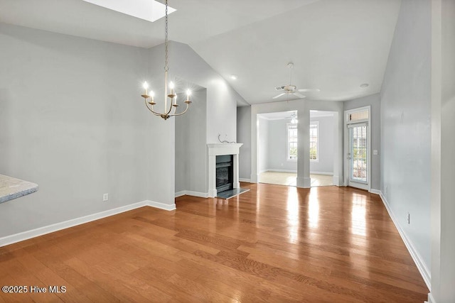 unfurnished living room with hardwood / wood-style flooring, ceiling fan with notable chandelier, and vaulted ceiling