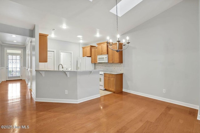 kitchen with light stone countertops, white appliances, tasteful backsplash, kitchen peninsula, and a breakfast bar