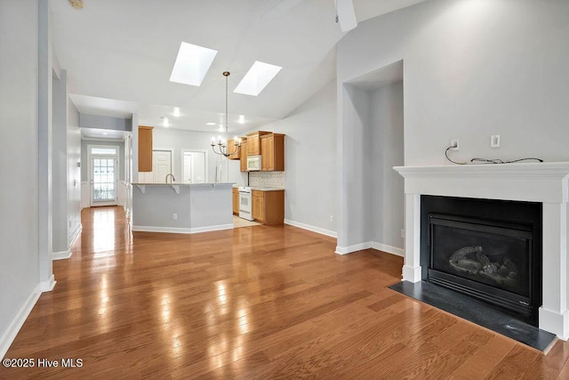 unfurnished living room featuring light wood-type flooring, a notable chandelier, and vaulted ceiling with skylight