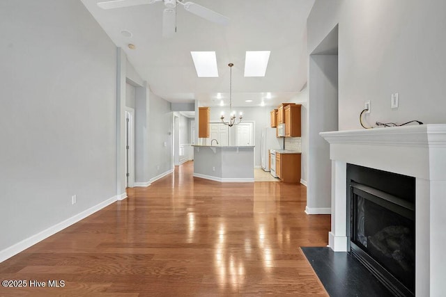 living room featuring a skylight, ceiling fan with notable chandelier, and light hardwood / wood-style flooring