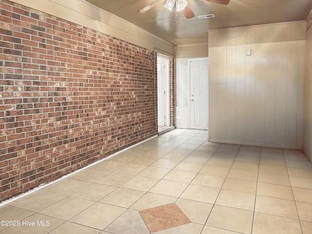 tiled spare room featuring ceiling fan and brick wall