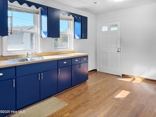 kitchen with blue cabinets, sink, a textured ceiling, and light hardwood / wood-style floors