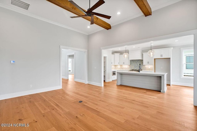 unfurnished living room with light hardwood / wood-style floors, sink, ornamental molding, ceiling fan, and beam ceiling