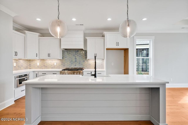 kitchen featuring wall chimney range hood, a center island with sink, and stainless steel oven