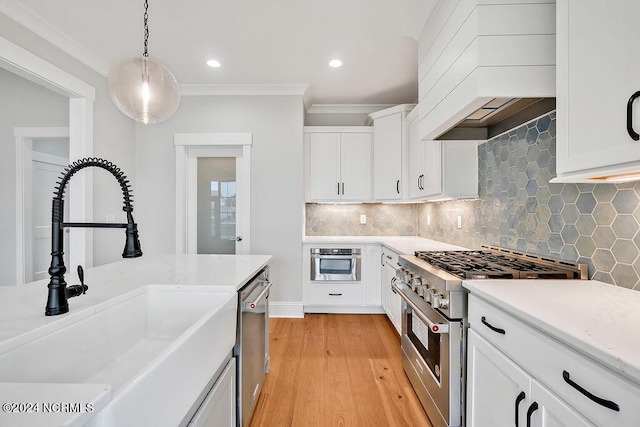 kitchen featuring premium range hood, white cabinetry, appliances with stainless steel finishes, pendant lighting, and sink