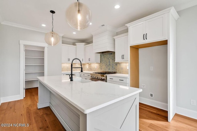 kitchen featuring decorative light fixtures, sink, an island with sink, white cabinets, and light stone counters