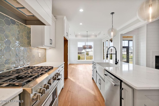 kitchen featuring custom exhaust hood, stainless steel appliances, a kitchen island with sink, pendant lighting, and white cabinets