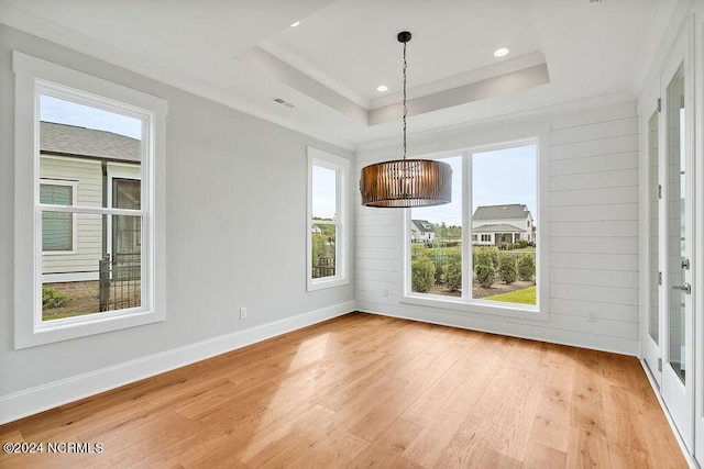 unfurnished dining area with a raised ceiling, light wood-type flooring, and ornamental molding