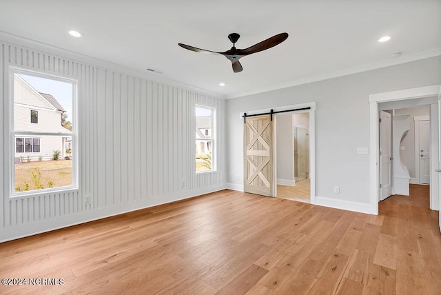 unfurnished bedroom with light wood-type flooring, ceiling fan, crown molding, and a barn door