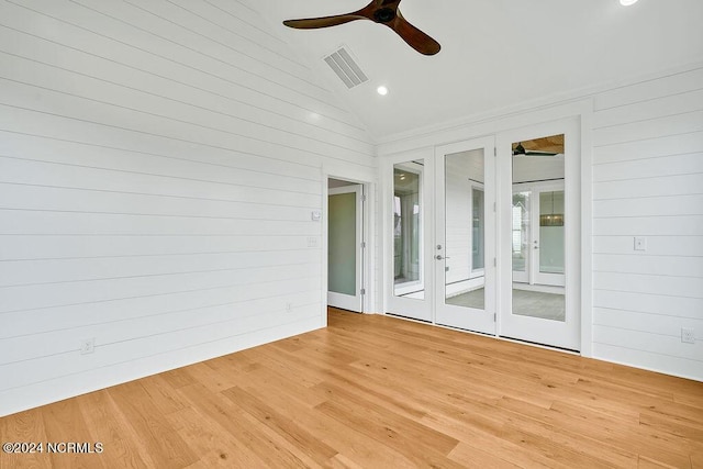 empty room with ceiling fan, wood walls, lofted ceiling, and light wood-type flooring